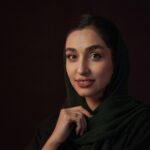 Beautiful portrait of a smiling woman in a dark green headscarf, set against a dark background.
