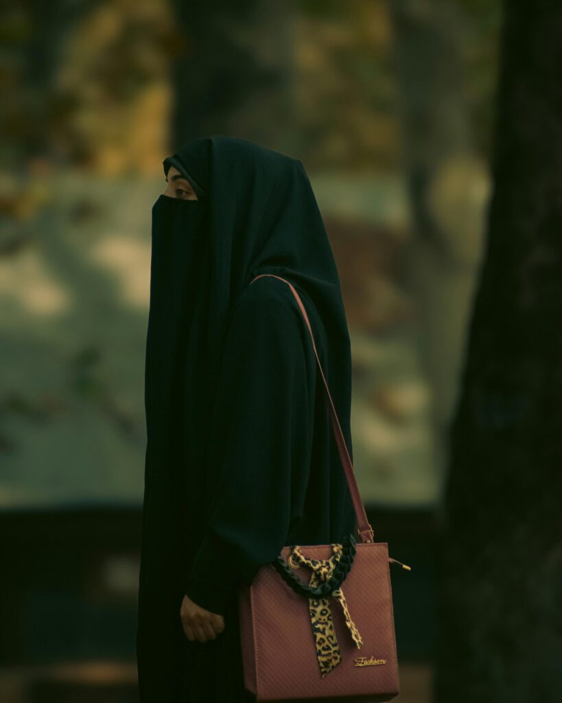 Side view of a Muslim woman in niqab walking outdoors in a park setting.